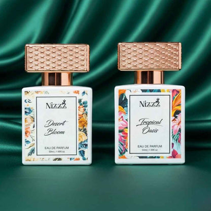 Two floral perfume bottles, Desert Bloom and Tropical Oasis, with rose gold caps on green satin background