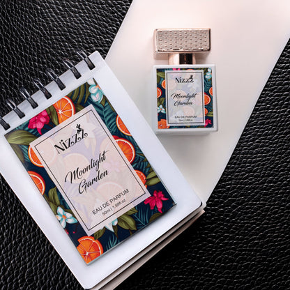 Nizzz Moonlight Garden Eau de Parfum bottle and notebook with floral citrus design on black leather