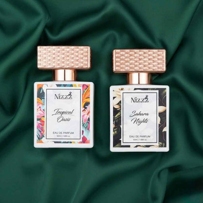 Two floral perfume bottles, Tropical Oasis and Sahara Nights, with rose gold caps on green fabric