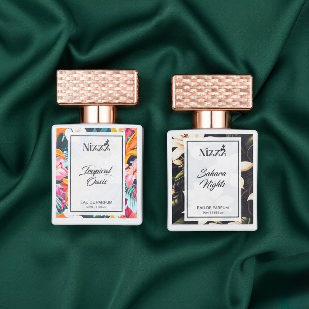 Two floral perfume bottles, Tropical Oasis and Sahara Nights, with rose gold caps on green fabric